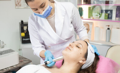 Naklejka premium Woman is getting her face done by a doctor. The doctor is wearing a white coat and a blue mask. The woman is lying on a bed and the doctor is using a device to clean her face