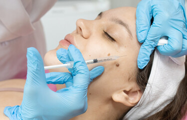 Fototapeta premium Woman is getting injection in her face. The woman is wearing blue gloves.