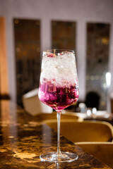 Colorful and refreshing, a cocktail glass filled with ice and vibrant hues sits on a lavish bar. The ambiance suggests a cozy night out, perfect for socializing and unwinding with friends. 