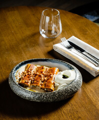 Delicate sweet rolls drizzled with golden honey and sprinkled with crushed pistachio sit on a textured plate. A refined glass waits nearby, enhancing the warm, inviting atmosphere of the moment. 