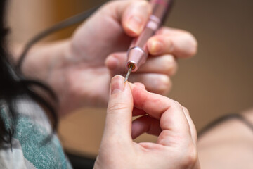 Obraz premium woman's hands using an electric nail file to smooth the edges of nails after cuticle removal, showcasing a professional manicure process