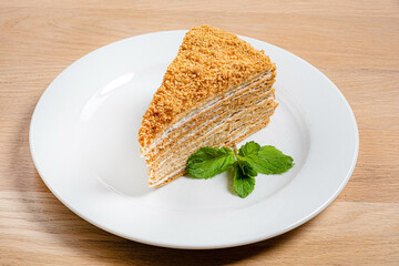 A luscious slice of honey cake is presented elegantly on a white plate, adorned with vibrant mint leaves. The cake’s layered texture invites indulgence and delight. 