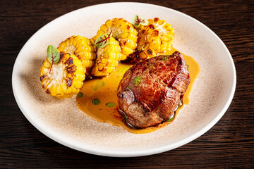 Juicy pork tenderloin rests on a bed of rich sauce, accompanied by sweet, charred corn. Fresh herbs add vibrant color and flavor, creating an enticing dish perfect for a special meal. 
