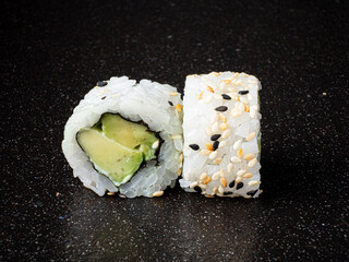Two beautifully made sushi rolls display creamy avocado nestled in soft rice, adorned with sesame seeds. The contrasting colors create an inviting, appetizing scene perfect for food lovers. 