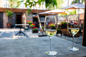Two elegant wine glasses filled with golden drink rest on a textured table, encircled by colorful flowers and warm sunlight, creating a serene ambiance perfect for relaxation. 