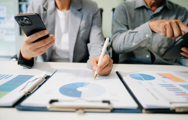 Business documents on office table with smart phone and laptop and two colleagues discussing data