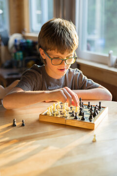 Young boy at sunlit table plays next move in game of chess