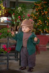 arafed toddler in a green jacket and brown hat standing in front of a wooden chair
