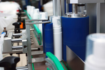 White plastic bottle is moving along conveyor belt. Capping and labeling machine. Production of cosmetics and skin care products.