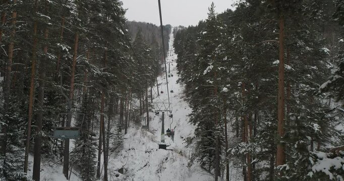 Transport. People sitting on the seats climb the funicular lift up the mountain among the snow-covered pine forest. Hand held. Siberia.