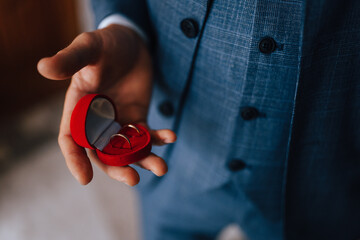The groom in a suit holds wedding rings in his hand