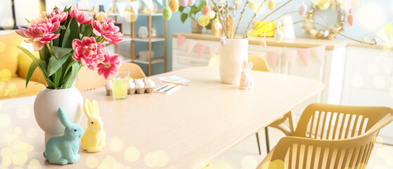 Vase with tulip flowers and toy bunnies on table in decorated kitchen. Easter celebration