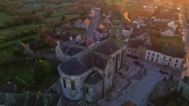 Eglise Saint-Gervais et Saint-Protais, church, Jublains town at sunset, Mayenne in France. Aerial drone top-down orbiting