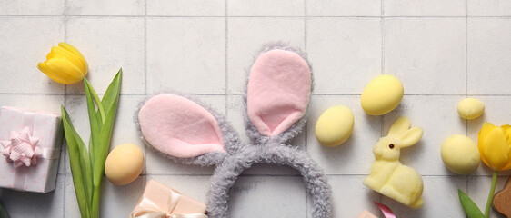 Bunny ears with Easter eggs, tulip flowers and gift boxes on white tiled background