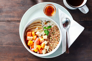 A healthy granola bowl with yogurt, mango, papaya, banana, honey, coconut flakes, and flax seeds. Served with a glass of water and a cup of coffee, creating a perfect balanced breakfast