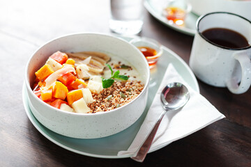 A healthy granola bowl with yogurt, mango, papaya, banana, honey, coconut flakes, and flax seeds. Served with a glass of water and a cup of coffee, creating a perfect balanced breakfast