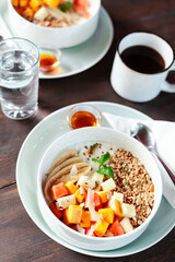 A healthy granola bowl with yogurt, mango, papaya, banana, honey, coconut flakes, and flax seeds. Served with a glass of water and a cup of coffee, creating a perfect balanced breakfast