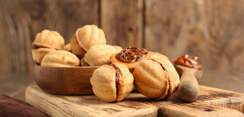 Cutting board and bowl of sweet walnut shaped cookies with boiled condensed milk on wooden background