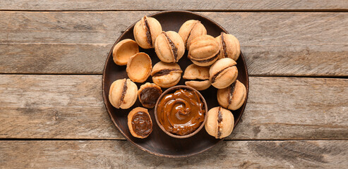 Plate with sweet walnut shaped cookies with boiled condensed milk on wooden background