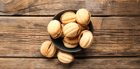 Bowl of sweet walnut shaped cookies with boiled condensed milk on wooden background