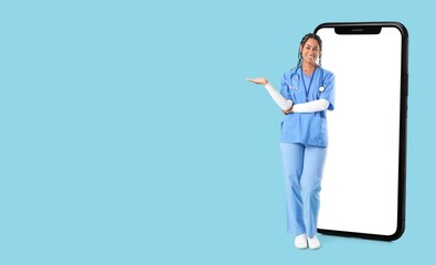 Big smartphone and young African-American female doctor on light blue background with space for text