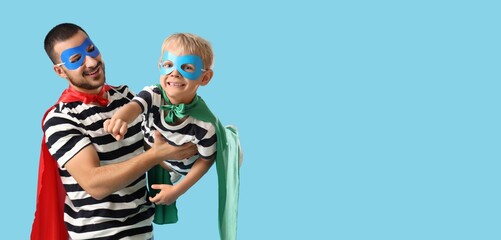 Happy father and his little son dressed as superheroes on light blue background with space for text