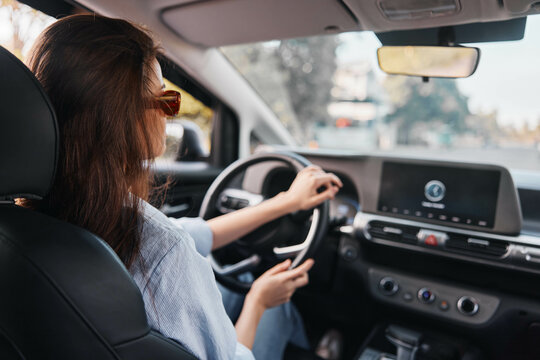 Woman driving car, hands on steering wheel, eyes focused on dashboard screen, interior view
