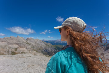Portrait from behind of young woman in sunglasses with hair blowing in the wind who is hiking outdoors in mountains, Latemar, Trentino, Italy. Traveling concept photography and outdoor sport activity