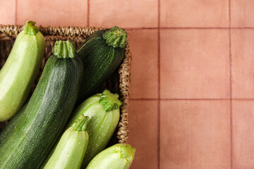 Wicker basket with raw zucchini on beige tile background