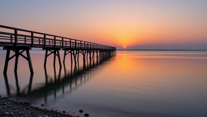 Obraz premium Serene Sunrise over Calm Water with Long Pier Extending to Horizon