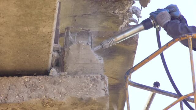Construction worker using heavy-duty jackhammer tool and breaking reinforced concrete. Under construction. Close up view of heavy-duty jackhammer crushing concrete. Construction worker holding
