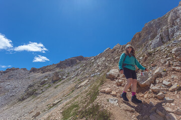 Young woman with sunglasses, long air and cap walking in the middle of dolomite peaks, Latemar, Trentino, Italy. Traveling photography and outdoor sport activity concept