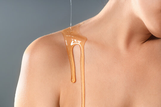 Young woman with dripping honey on collarbone against grey background, closeup