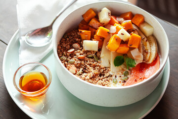 A healthy granola bowl with yogurt, mango, papaya, banana, honey, coconut flakes, and flax seeds. Served with a glass of water and a cup of coffee, creating a perfect balanced breakfast