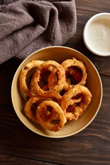 Crispy fried onion rings in bowl on wooden table