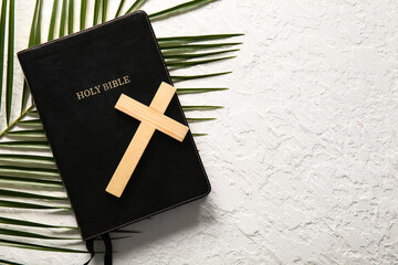 Wooden cross with palm leaf and Holy Bible on white background