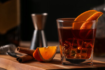 Board with glass of Old Fashioned Cocktail, orange slices and cinnamon sticks, closeup