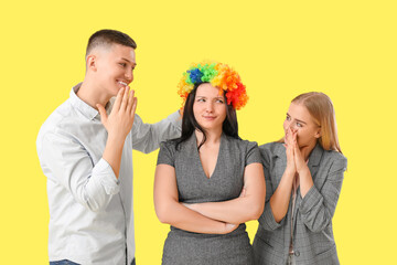 Business people putting clown wig on their colleague against yellow background. April Fools' Day celebration