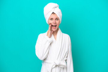 Young woman in a bathrobe isolated on blue background with surprise and shocked facial expression