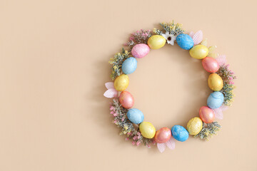 Wreath made from Easter eggs and flowers hanging on beige wall, closeup