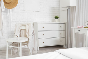Interior of light bedroom with chair, drawers and lamp
