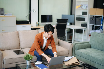 Confident young businessman working on a laptop, analyzing documents in a stylish modern office.