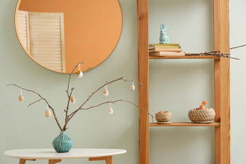 Vase with tree branches and Easter eggs on table in room