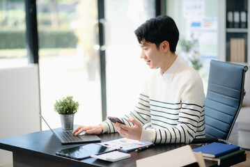 Fototapeta premium Confident businessman working on finance analysis with a tablet and laptop at office desk.
