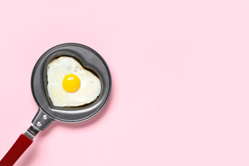 Frying pan with heart-shaped fried egg on pink background