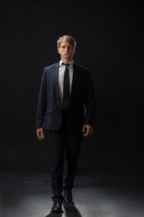 confident man strides forward in a dark suit, exuding authority and professionalism. The low-key, dark background highlights the formal attire in a corporate setting