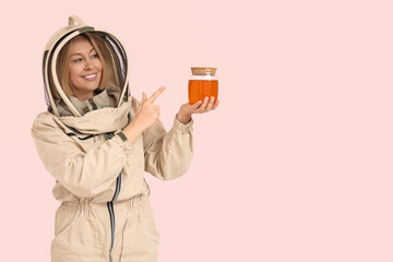 Female beekeeper pointing at jar of sweet honey on pink background