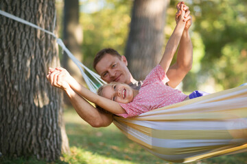 dad hugs d child daughter swing in a hammock in a summer park or garden. Concept of friendly family.