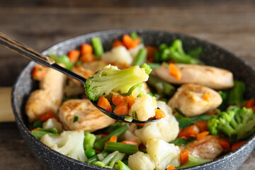 Frying pan with tasty chicken fillet and vegetables on wooden table, closeup