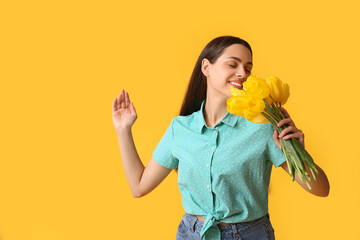 Beautiful young happy woman with bouquet of tulip flowers on yellow background